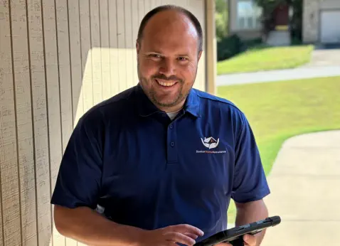 Senior Home Assurance representative holding iPad smiling at client door