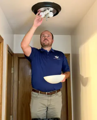 Senior Home Assurance representative changing light bulb on fixture