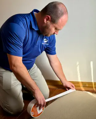 Senior Home Assurance representative applying rug tape to loose rug
