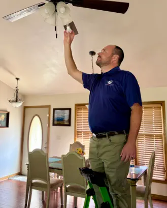Senior Home Assurance representative changing light bulb on ladder